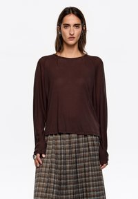 Bruine lange mouwen top met een ontspannen pasvorm en ronde hals, gecombineerd met een geruite geplooide rok in aardetinten en afwisselende strepen.