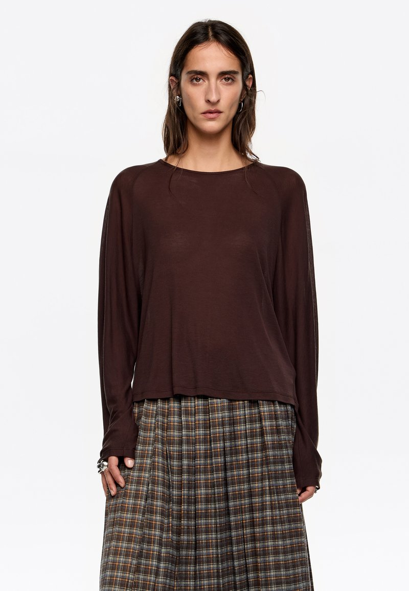 Bruine lange mouwen top met een ontspannen pasvorm en ronde hals, gecombineerd met een geruite geplooide rok in aardetinten en afwisselende strepen.