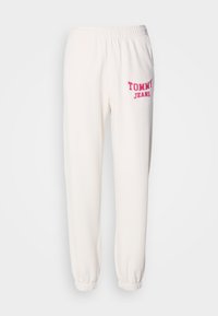 Witte trainingsbroek van zachte stof met een elastische tailleband, voorzien van een roze "TOMMY JEANS" logo aan de linkerkant en met cuffs bij de enkels.