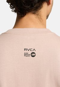 Light pink cotton t-shirt featuring a rounded neckline and a printed logo design on the back with the text "RVCA Artist Network Program."