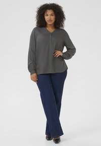 Blouse grise à manches longues et boutonnée avec un décolleté en V, associée à un jean évasé en denim foncé. Tissu doux, coupe décontractée et design basique.