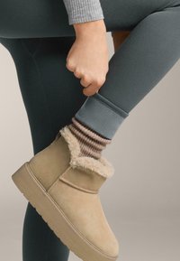 Barna bokacsizma bolyhos béléssel; zöld bordás leggings és egy szürke, bélés nélküli zokni bézs és barna csíkos mintával.