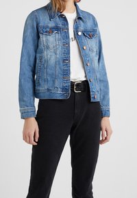 Džínová bunda v světle modré barvě s klasickým střihem, která má dvě náprsní kapsy, měděné knoflíky a lehce vybledlý vzhled. Nosená přes bílou košili a černé kalhoty.