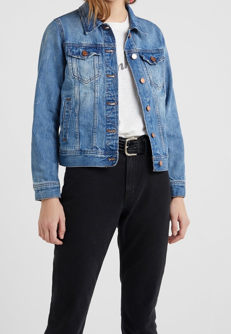 Džínová bunda v světle modré barvě s klasickým střihem, která má dvě náprsní kapsy, měděné knoflíky a lehce vybledlý vzhled. Nosená přes bílou košili a černé kalhoty.