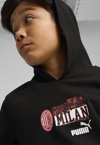 Felpa nera con cappuccio caratterizzata da un grande grafica rossa e bianca "Forza Milan", un emblema dell'AC Milan, e il logo Puma sul davanti.