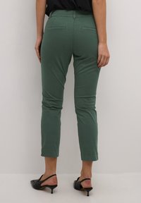 Zelené středně vysoké capri kalhoty s elastickým pasem. Obsahují dvě zadní kapsy a úzký střih, doplněné černými sandály na podpatku.