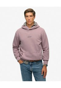 Sudadera morada con un bolsillo frontal, con un logotipo. Debajo, se ve una camisa de cuadros. Se lleva con jeans azules y un reloj.