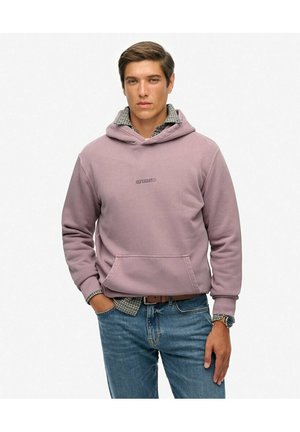 Felpa viola con tasca frontale, caratterizzata da un logo. Sotto, è visibile una camicia a scacchi. Indossata con jeans blu e un orologio.