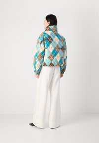 Polstret jakke med et flerfarvet argyle-mønster i turkis, brun og creme. Høj krave, elastiske manchetter og cropped design.