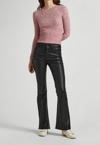 Maglia rosa a coste con maniche lunghe abbinata a pantaloni in pelle neri a campana e sneakers bianche. La maglia presenta un collo rotondo e un design aderente.