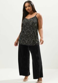 Svart bebands cami-top med ett fläktmönster och tunna remmar, parat med vida svarta sammetbyxor och klacksandaler.