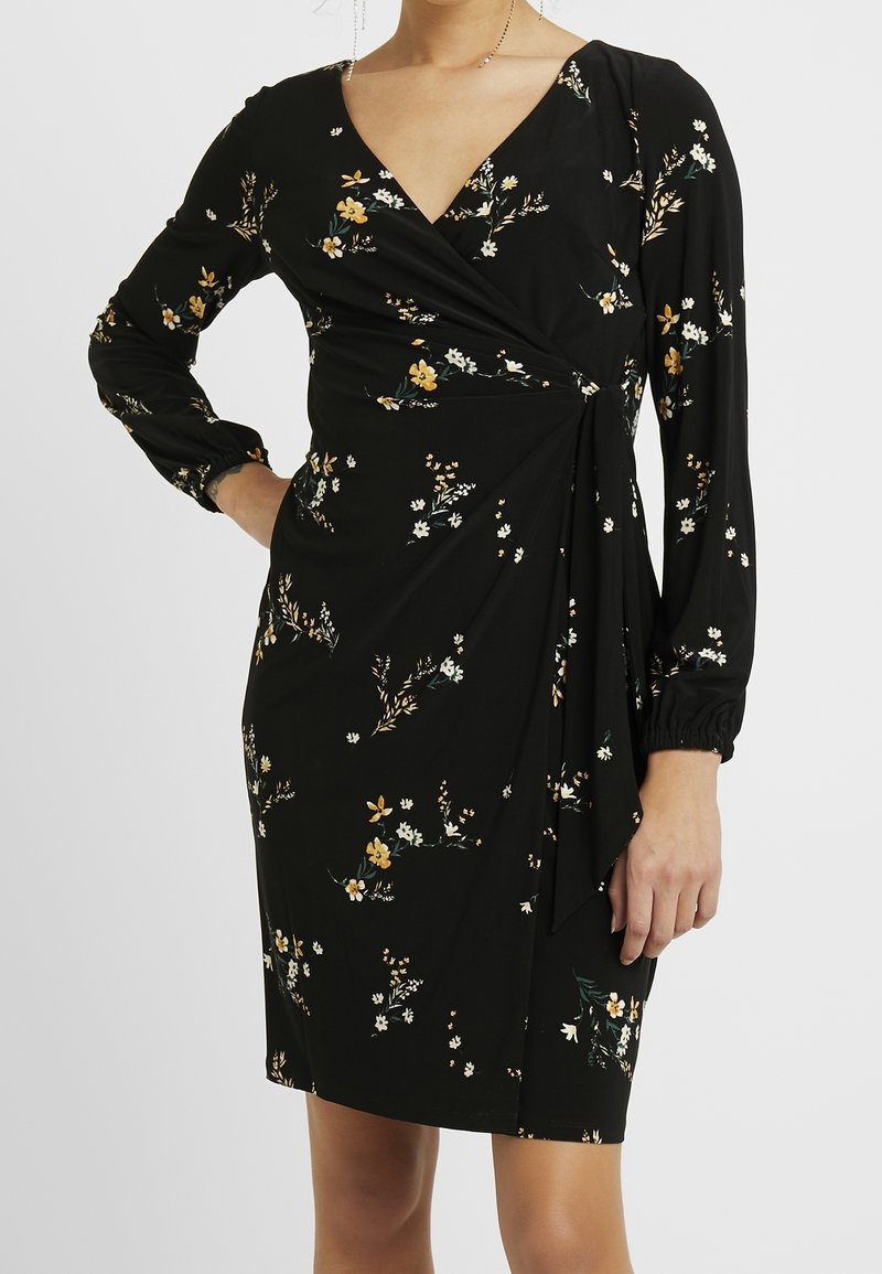 Svart omlottklänning med långa ärmar, V-halsringning och ett blommönster av vita och gula blommor. Mjuk tyg med en slät yta.