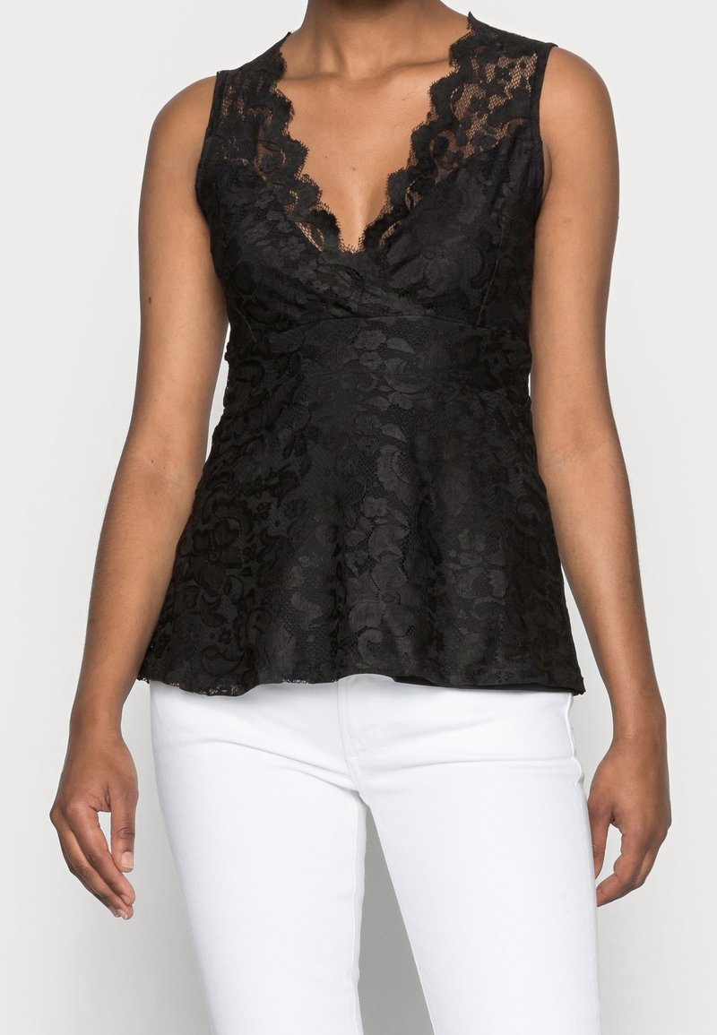 Top en dentelle noire à peplum avec un décolleté en V profond et des bords festonnés. Présente des motifs floraux et une taille ajustée qui s'évase au bas.