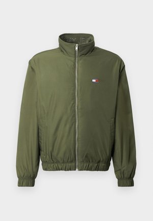 Olivno zeleni bomberski jopič z visokim ovratnikom, sprednjim zadrgo, elastičnimi manšetami in pasom. Ima majhen logotip na prsih.