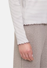 Gestreiftes langärmeliges Oberteil in Weiß und Hellbraun mit Rüschensäumen, kombiniert mit beigefarbenen Herringbone-Stoffhosen mit Struktur.