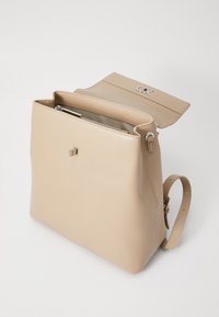 Beige lærryggsekk med en strukturert form, glidelåslukking og klaff. Har et sølvfarget logo og justerbar skulderstrop.