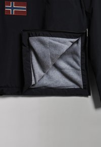 Zwarte jas met een Noorse vlagpatch; de opengebroken zak toont een zachte grijze voering, wat het contrast in textuur en kleur benadrukt.