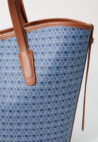 Blue patterned tote bag with a textured canvas surface and brown leather accents. Features sturdy handles and a spacious design.