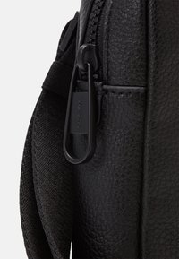 Borsa nera con cerniera, caratterizzata da una texture in pelle martellata, dettagli in tessuto intrecciato e una clip robusta. Il design enfatizza funzionalità e durabilità.