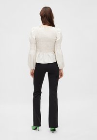 Vit smockblus med puffärmar, i kombination med svarta byxor. Modellen bär gröna klackar, vilket framhäver den unika färgkontrasten.