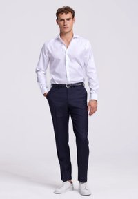 Witte lange mouwen shirt, donkerblauwe broek, zwarte riem en witte sneakers. Slank ontwerp met een soepele textuur. Geen patronen of accenten.