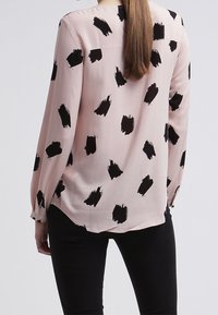 Blusa a maniche lunghe in morbido tessuto rosa chiaro, caratterizzata da un motivo a pennellate nere. Taglio con orlo arrotondato e vestibilità comoda.