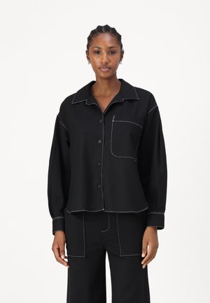 Schwarze Button-Up-Hemd mit Kragen, mit weißen Kontrastnähten, langen Ärmeln und einer Brusttasche. Glatte Stofftextur.