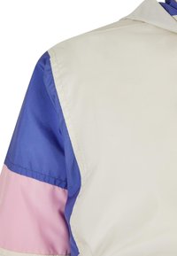 Flerfarget vindjakke med en hvit øverste del, kongeblå ermer og rosa stripe, laget av glatt, lett stoff.