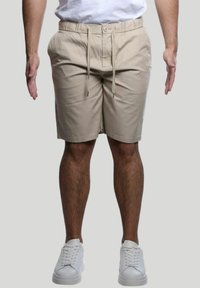 Pantaloni casual beige realizzati in tessuto misto cotone, con vita a coulisse, tasche laterali e taglio dritto. Indossati con sneakers bianche.