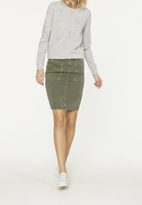Sweatshirt gris avec des motifs d'étoiles et de soleil, associé à une jupe en denim olive près du corps. Le modèle porte des baskets blanches.