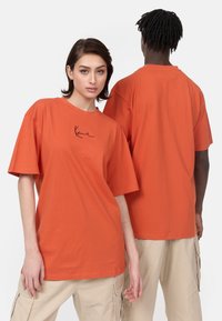 Oversized orange t-shirt lavet af bomuld, med en let texture og et enkelt sort signaturlogo på fronten. Casual pasform.