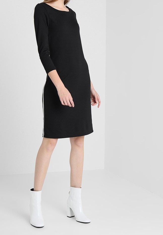 Svart klänning med trekvartslånga ärmar, med vita sidostreck; tillsammans med vita ankelskor, slät textur och enkel design.