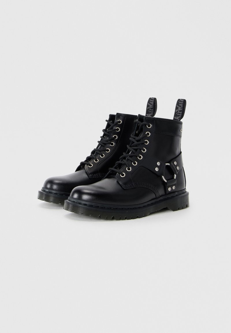 Bottines en cuir noir avec œillets en métal, semelle épaisse et détail de sangle sur le côté. Dotées de languettes de tirage pour un enfiler facile et d'une texture lisse.