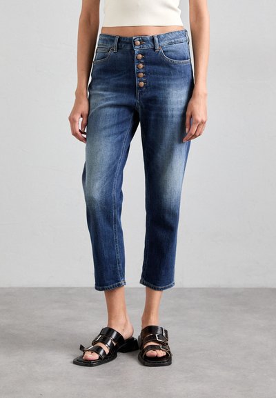 Blå højtaljede denim jeans med en fem-knaps lynlås, cropped længde og let lysning. Bærer sorte sandaler med åbne tæer.