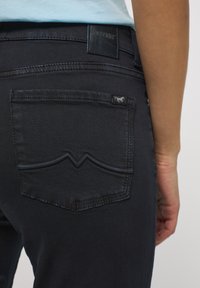 Sötétkék farmernadrág, texturált anyaggal, hátul található zseb kiemelkedő varrásmintával és fekete bőrből készült márkajelzéssel.