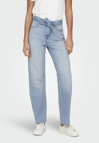 Jasnoniebieskie, wysokiej talii dżinsy z wiązanym paskiem, proste nogawki, delikatne przetarcia, pięć kieszeni oraz postrzępiony dół, w zestawie z białymi trampkami.