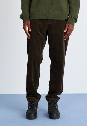 Brown corduroy pants with a straight cut, paired with black lace-up boots. A green knit sweater with ribbed cuffs completes the outfit.