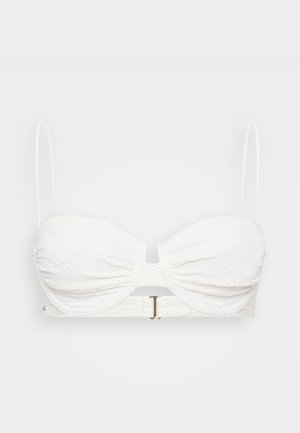 Haut de bikini bandeau blanc en tissu texturé, avec des coques courbées et des bretelles spaghetti réglables ; présente un fermoir en ton doré à l'arrière.