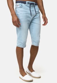 Pantalones cortos de mezclilla capri de color azul claro con cintura elástica, cordón en tono navy y bolsillos laterales, que presentan un ligero desgaste y dobladillos rematados.