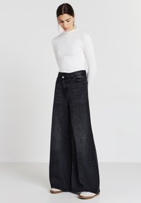 Jean noir à jambe large avec une taille haute, associé à un haut ajusté à manches longues blanc à côtes. La tenue présente un design minimaliste et des tons neutres.