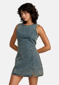 Denim mekko, jossa on hihaton muotoilu, haalistunut sininen väri, sivuhalkiot ja kontrastiväriset ompeleet. Silkkinen pinta ja vartalonmyötäinen siluetti.