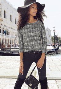 Top a scacchi bianco e nero con maniche a tre quarti, jeans neri, stivali neri al ginocchio e un cappello nero a tesa larga. Include una borsa decorata con borchie.