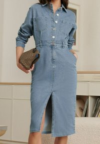 Abito camicia in denim con maniche lunghe, chiusura a bottoni sul davanti, due tasche sul petto, vita contrassegnata da una cintura e spacco anteriore, in un lavaggio azzurro chiaro.