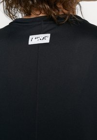 Camiseta deportiva negra con una pequeña etiqueta de logo bordada en la parte posterior del cuello y un tejido suave y elástico con costuras mínimas.