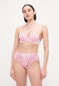 Lichtroze lingerie set met een gevormde beha versierd met kleine rode hartapplicaties en bijpassende hipster slip met kantafwerking en hartdetails.