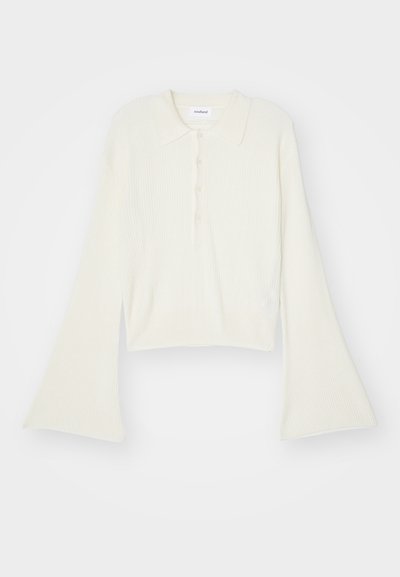 Prążkowana, kremowa koszulka polo z długimi, rozszerzającymi się rękawami i zapięciem na pięć guzików. Posiada kołnierz o miękkiej fakturze.