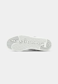Suela de zapatilla negra con goma blanca texturizada, con un diseño de banda de rodadura y un logotipo en relieve. Forma plana y redondeada con un talón reforzado.