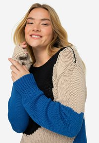 Maglione lavorato a maglia con un design color block in beige, nero e blu, con polsini a coste e una finitura testurizzata.