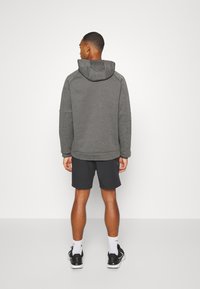 Sudadera gris con capucha, mangas largas y corte relajado; combinada con pantalones cortos oscuros. El material parece suave con una textura lisada.