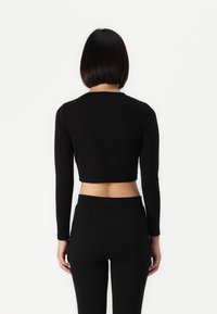 Black long-sleeve cropped top with a round neckline and fitted silhouette, paired with high-waisted black leggings, showing a smooth texture.